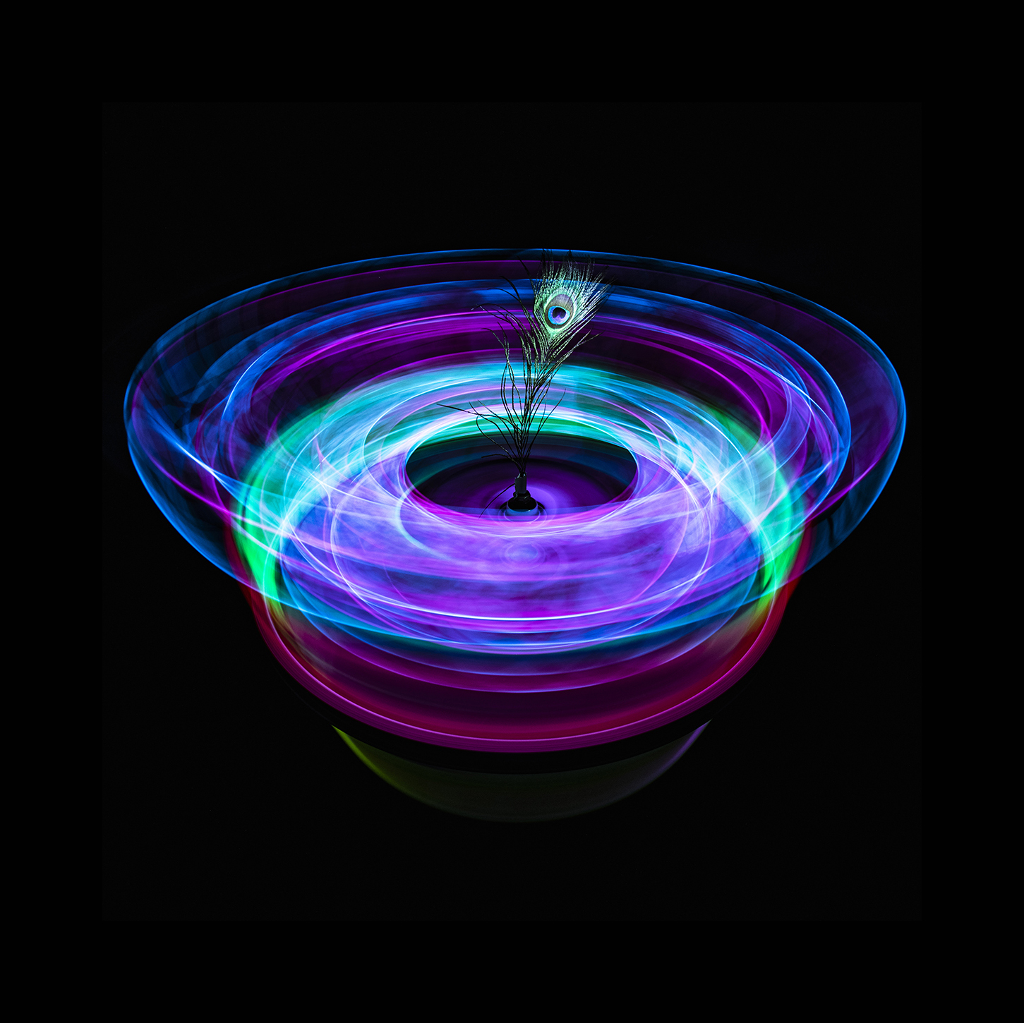 A bowl-shaped arrangement of blue, purple and turquoise light with a peacock feather